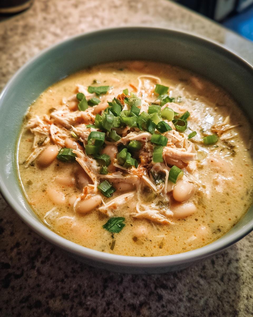 A close-up of a bowl of creamy White Chicken Chili, topped with shredded chicken and chopped green onions.