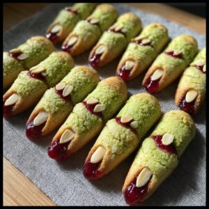 A close-up of several green witch finger cookies, decorated with almond slivers for nails and red jam for blood.