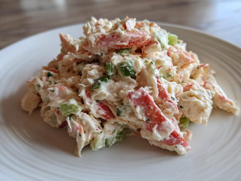 Close-up of a mound of creamy crab salad featuring imitation crab sticks and chopped celery on a white plate.