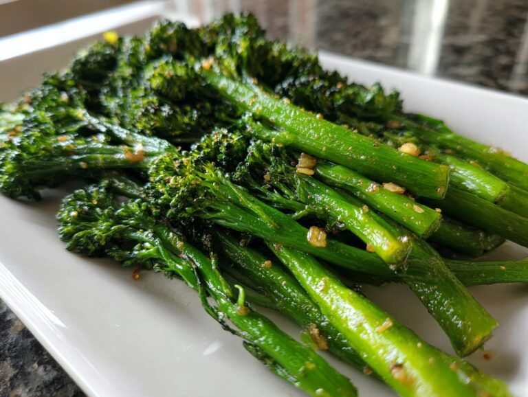 Close-up of vibrant green roasted broccolini seasoned with garlic bits, served on a white rectangular plate.