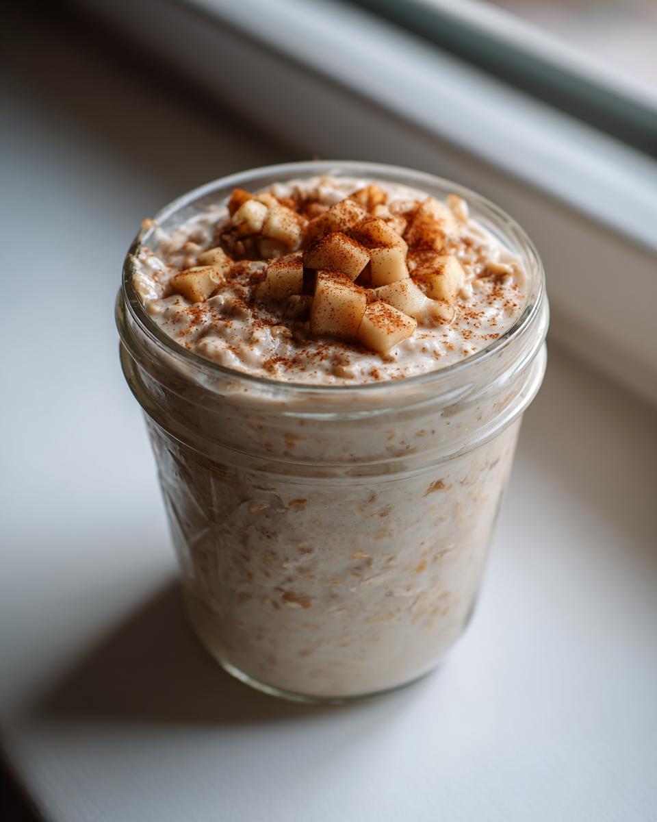 Close-up of apple cinnamon overnight oats in a glass jar, topped with diced apples and cinnamon.
