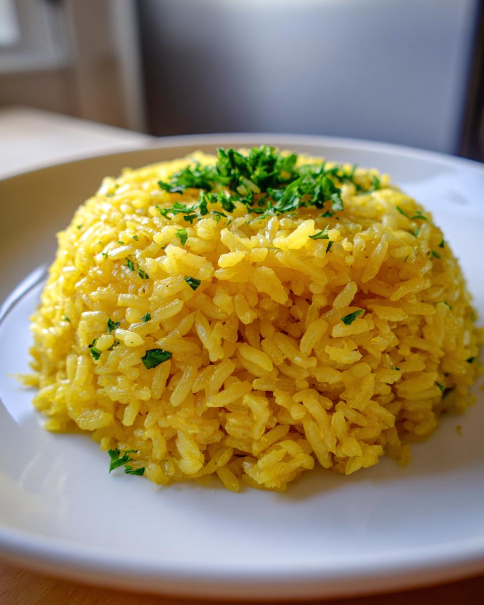A mound of bright yellow turmeric rice garnished with fresh chopped parsley on a white plate.