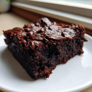 Close-up of a fudgy slice of date brownies topped with melted chocolate chips on a white plate.