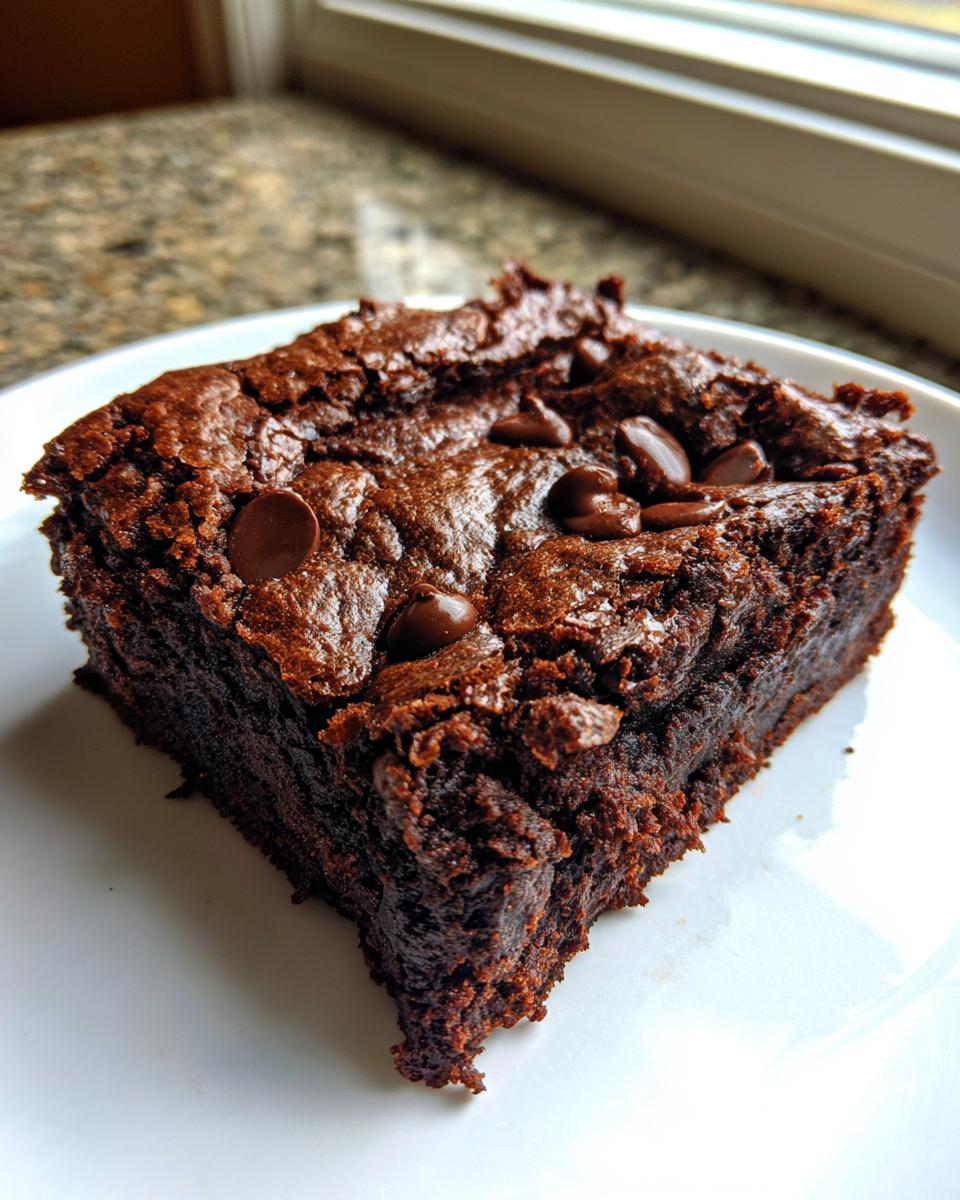 A close-up of a thick, fudgy slice of date brownies topped with melted chocolate chips on a white plate.