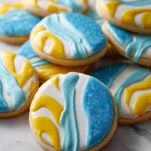 Close-up of round sugar cookies decorated with white, yellow, and blue cookie icing, some topped with blue sprinkles.
