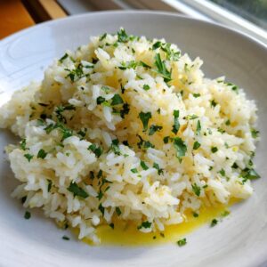 A close-up of fluffy white butter rice seasoned with melted butter and topped with fresh chopped parsley.