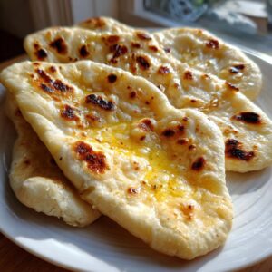 Close-up of fluffy homemade naan bread brushed with melted butter, showing charred spots.