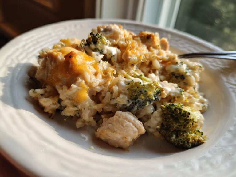 A close-up serving of creamy chicken broccoli rice casserole topped with melted cheddar cheese on a white plate.