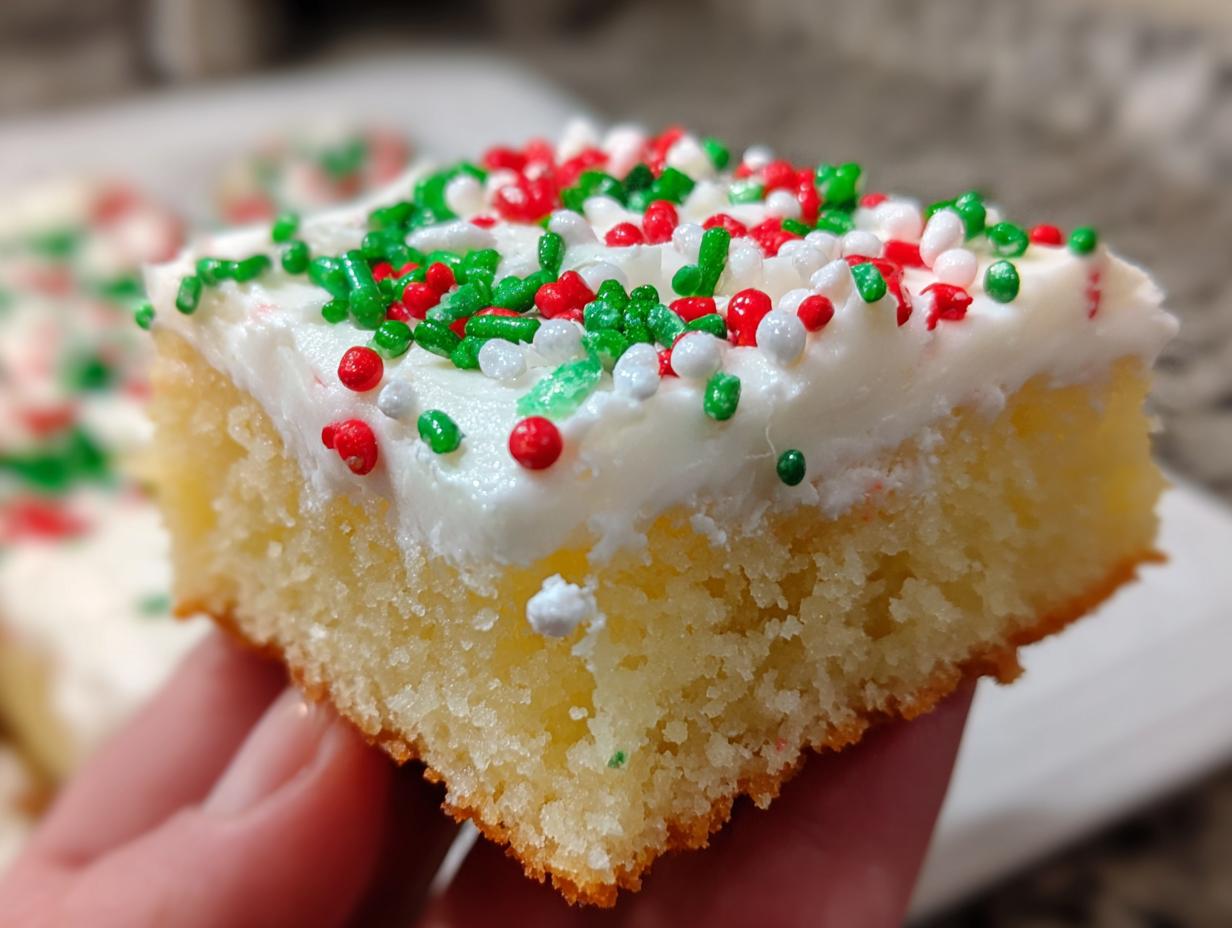 A close-up of a thick, soft slice of Christmas sugar cookie bars topped with white frosting and red, green, and white holiday sprinkles.