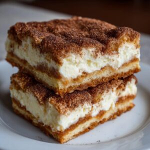 Two stacked squares of rich churro cheesecake bars topped generously with cinnamon sugar.