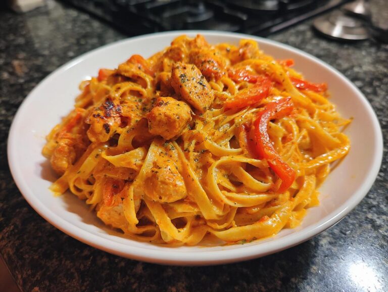 A close-up of creamy cajun chicken pasta featuring fettuccine, seasoned chicken pieces, and red bell peppers.