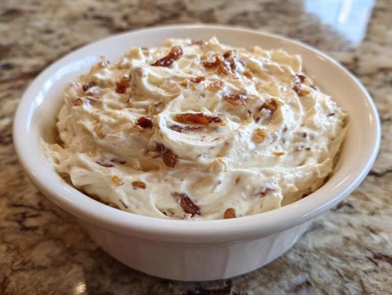 A white bowl filled with thick, creamy caramelized onion dip topped with crispy bacon pieces.