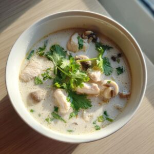 Overhead view of a creamy white bowl of coconut soup featuring chunks of chicken, sliced mushrooms, and fresh cilantro garnish.
