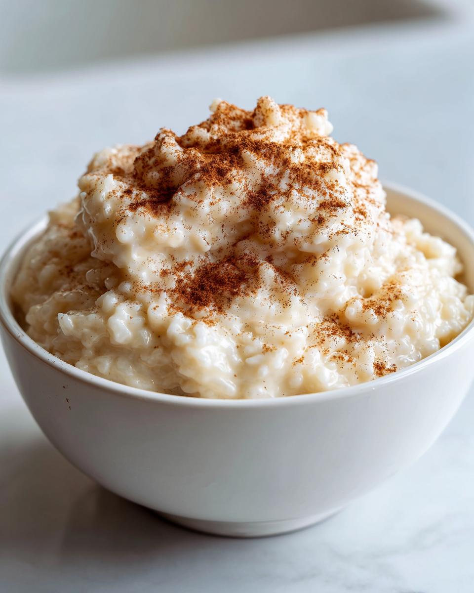 A close-up of creamy rice pudding recipe served in a white bowl, generously dusted with ground cinnamon.
