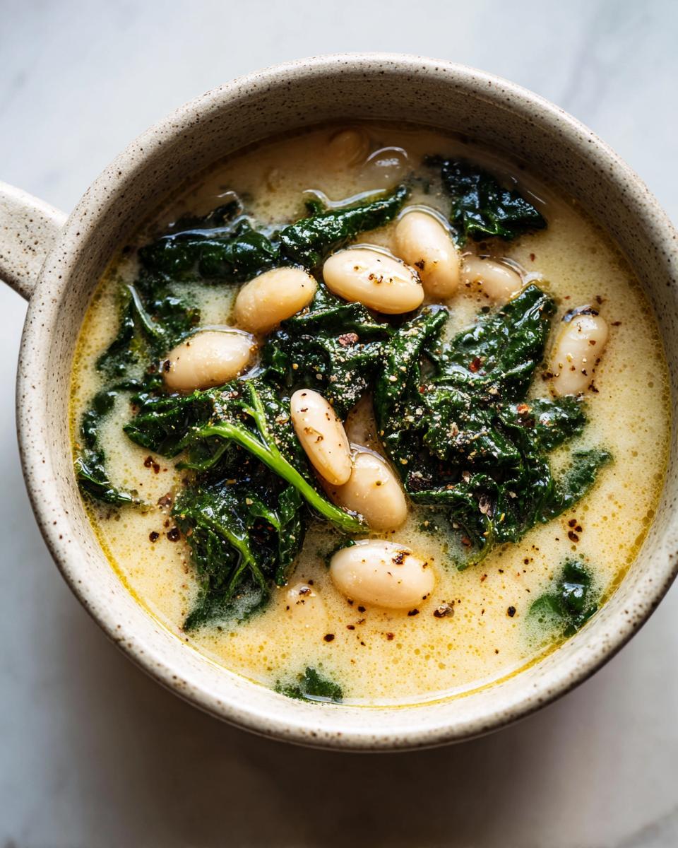 Overhead close-up of creamy Tuscan white bean soup featuring cannellini beans and dark green kale, seasoned with pepper.