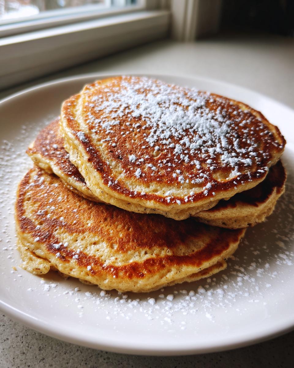 A stack of three fluffy oatmeal pancakes dusted generously with powdered sugar on a white plate.