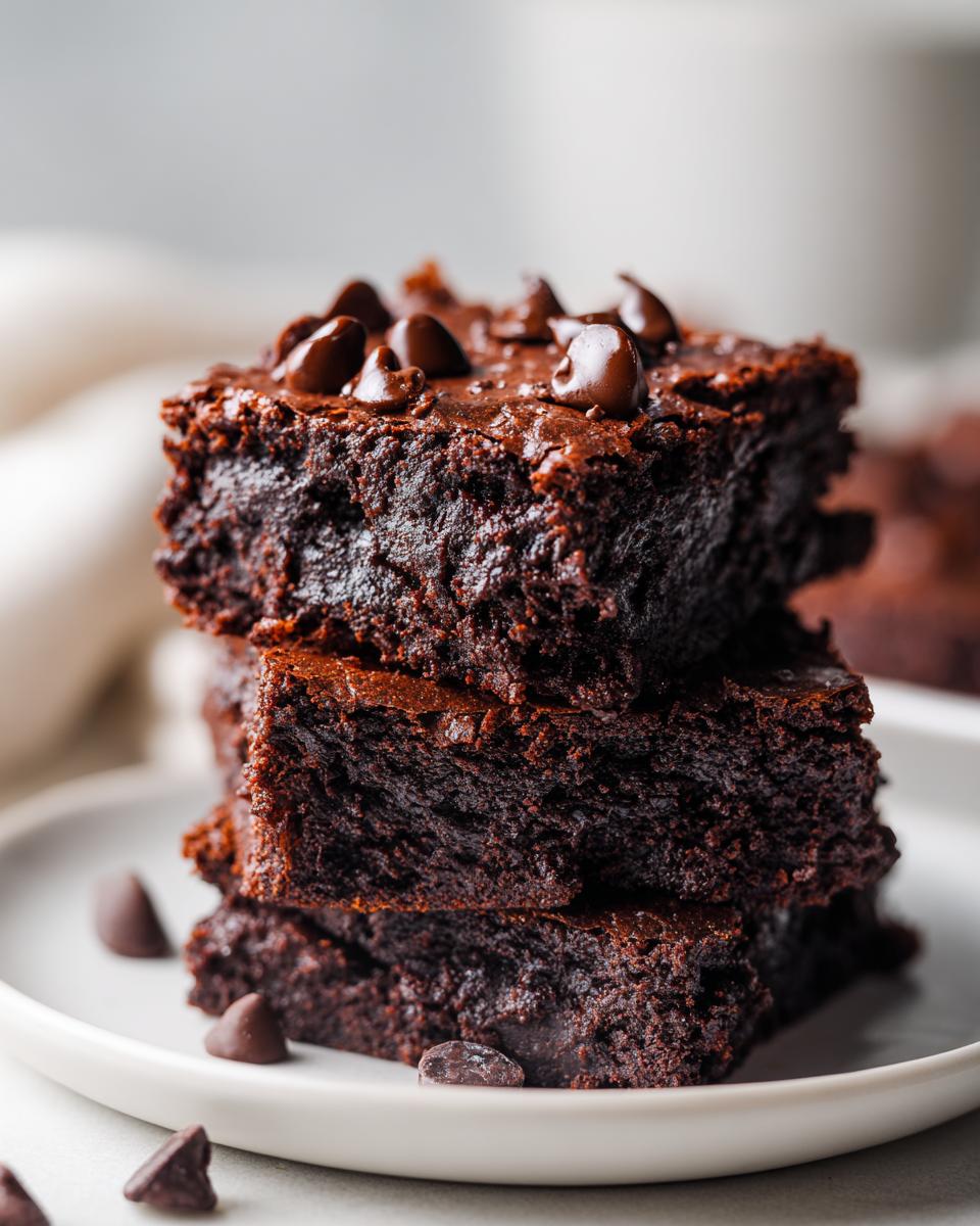 A stack of three rich, fudgy sweet potato brownies topped with melted chocolate chips on a white plate.
