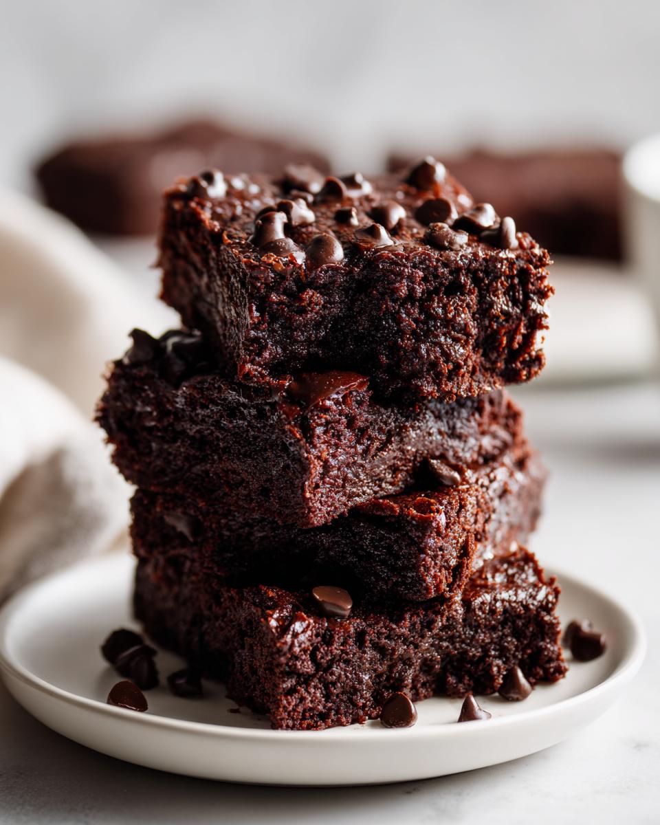 A stack of four fudgy sweet potato brownies topped with melted chocolate chips on a white plate.