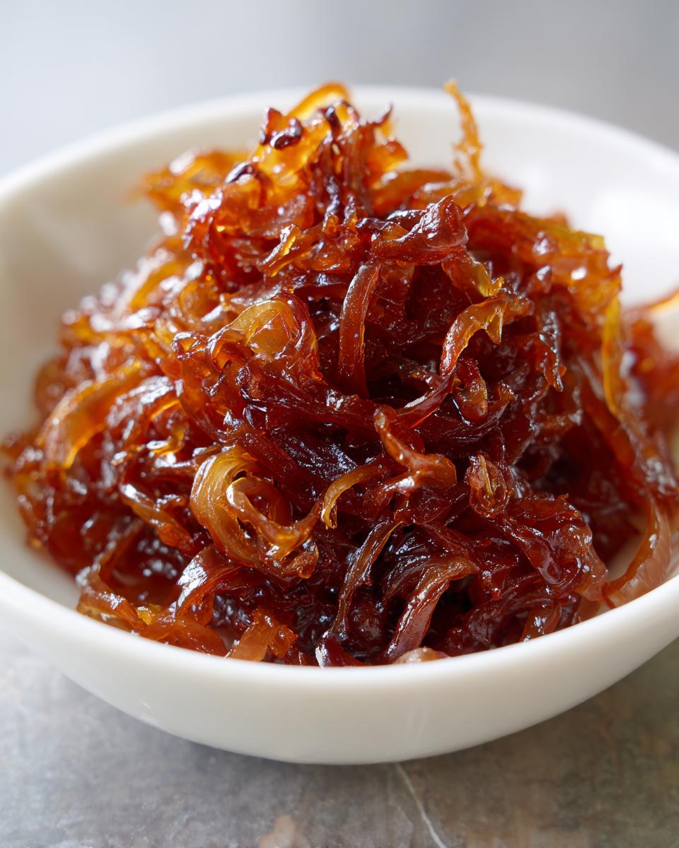 Close-up of deeply browned, glossy caramelized onions piled high in a small white serving bowl.