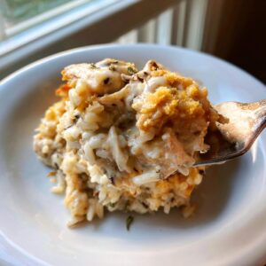 A fork lifting a creamy scoop of chicken wild rice casserole, showing rice, chicken chunks, and a crunchy topping.