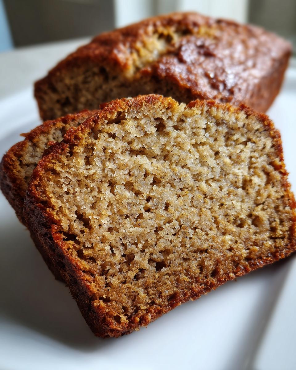 Two thick slices of moist sugar free banana bread showing a tender crumb texture, with the rest of the loaf blurred in the background.