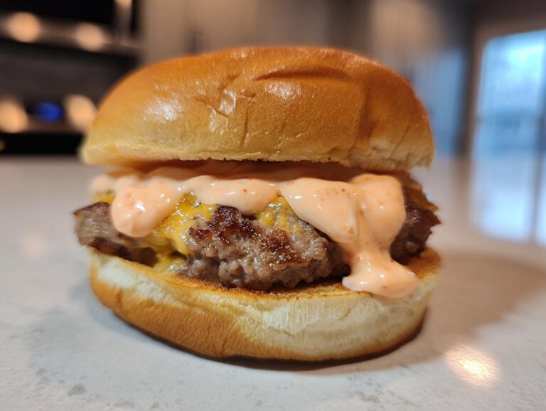 A close-up of a juicy smash burger topped generously with creamy, orange-pink smash burger sauce and melted cheese.