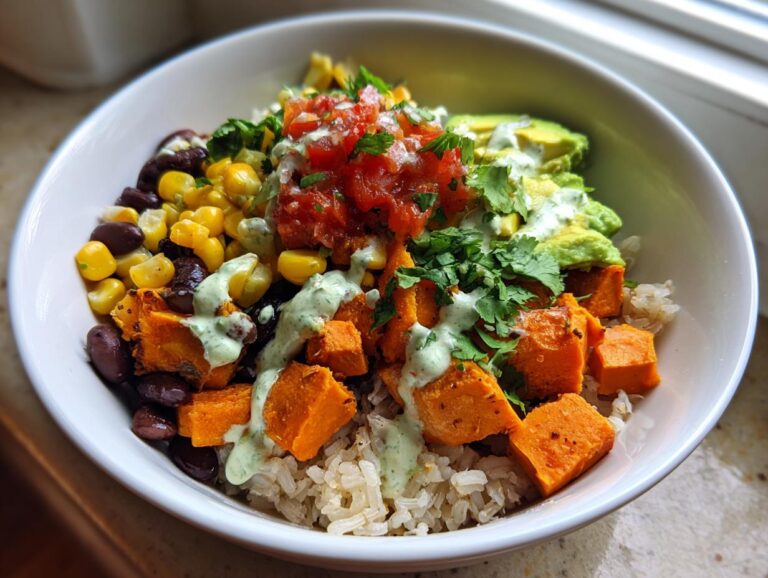 Close-up of a colorful sweet potato taco bowl featuring roasted sweet potatoes, black beans, corn, avocado, and a green cilantro sauce.