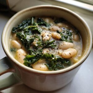 Close-up of a creamy tuscan white bean soup topped with wilted kale and cracked black pepper, served in a rustic mug.