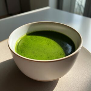 A close-up of a creamy, bright green bowl of homemade spinach soup sitting on a light-colored saucer.
