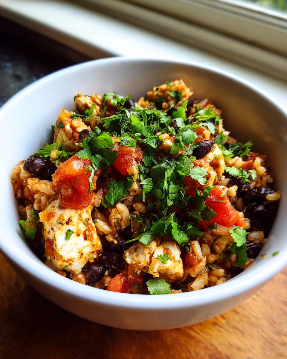 A close-up view of a vibrant chicken burrito bowl featuring seasoned chicken, rice, black beans, tomatoes, and fresh cilantro.