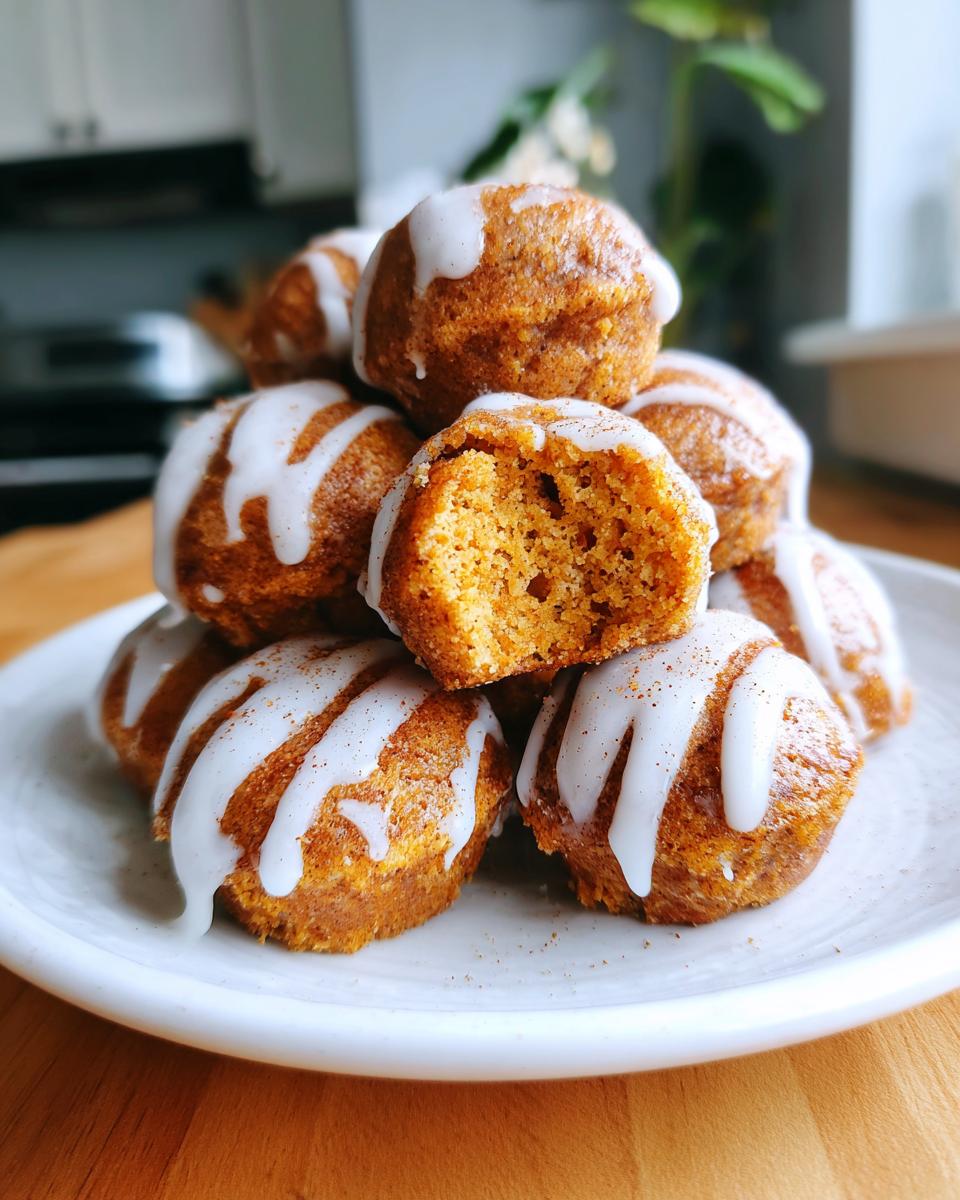 A stack of freshly baked, glazed cinnamon roll bites piled on a white plate, one is broken open.