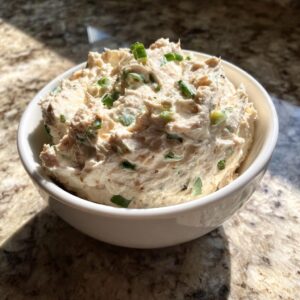 A white bowl filled with thick, creamy clam dip, garnished with chopped green onions.