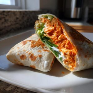 A delicious buffalo chicken wrap cut in half, showing shredded orange buffalo chicken, lettuce, and ranch dressing inside a toasted tortilla.