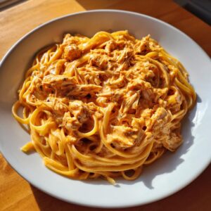 A close-up of a white bowl filled with creamy, orange-hued crab pasta, featuring linguine coated in a rich sauce.