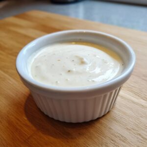 Close-up of creamy garlic sauce served in a small white fluted ramekin on a wooden surface.