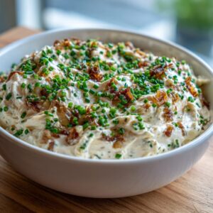 A close-up of a white bowl filled with creamy onion dip, garnished heavily with fresh green chives and crispy fried onions.