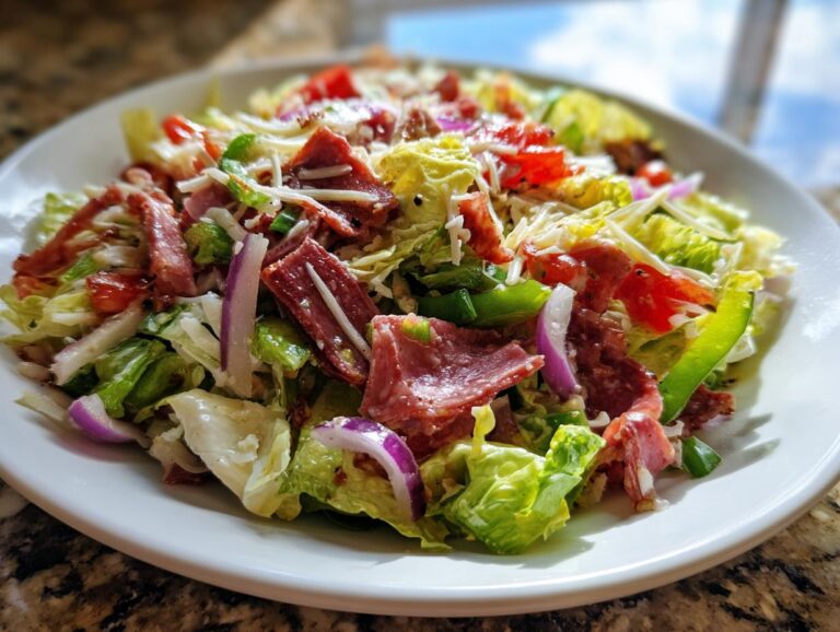 A vibrant, close-up shot of a fresh grinder salad featuring lettuce, salami, red onion, peppers, and shredded cheese.