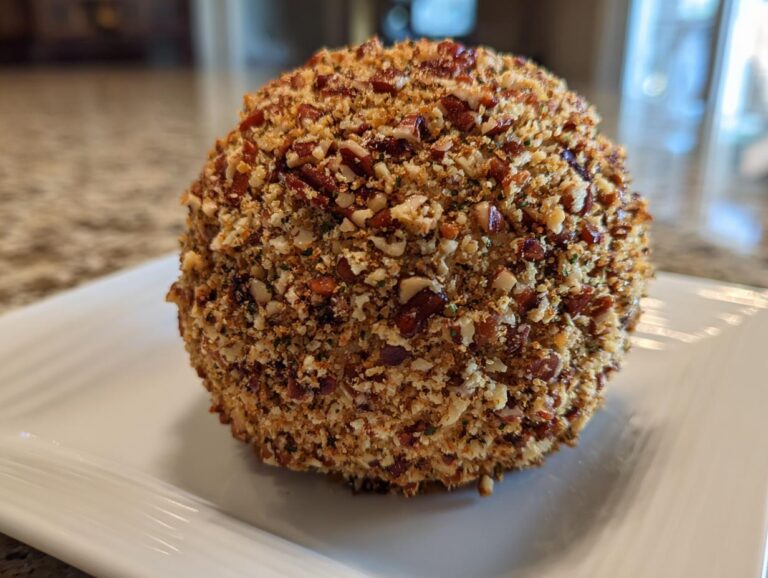 A close-up of a perfectly shaped cheese ball recipe coated entirely in chopped pecans and seasonings.
