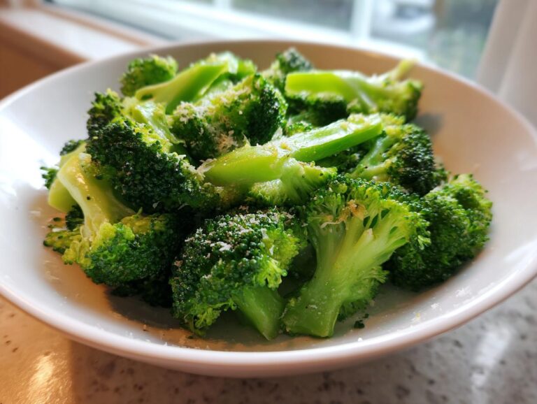 Bright green, perfectly steamed broccoli florets seasoned with grated Parmesan cheese in a white bowl.