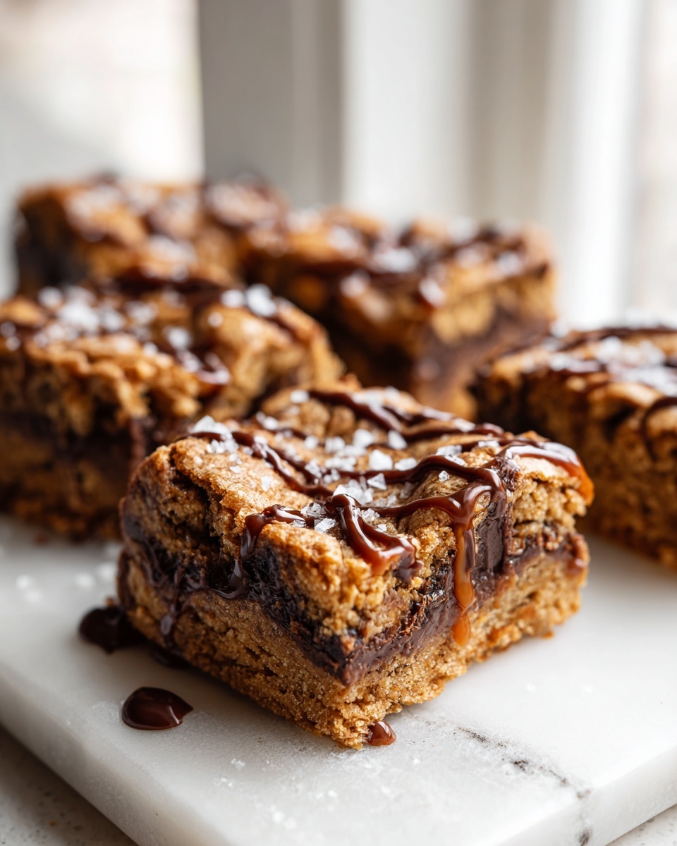 A close-up of thick, layered cookie bars drizzled with caramel and sprinkled with sea salt.