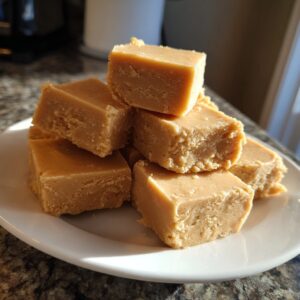 A close-up stack of creamy, light brown peanut butter fudge squares resting on a white plate.