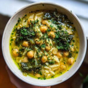 Overhead view of a bowl of amazing greek chickpea soup featuring chickpeas, orzo pasta, dark greens, and fresh parsley.