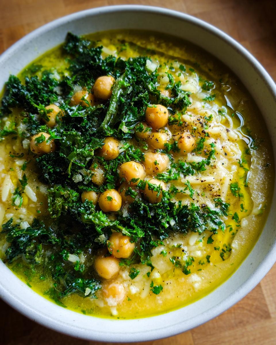 A close-up bowl of amazing greek chickpea soup topped with whole chickpeas, dark green cooked kale, and a drizzle of bright yellow olive oil.