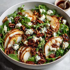 A close-up of an amazing pear salad featuring sliced pears, candied pecans, blue cheese crumbles, and arugula, drizzled with dressing.