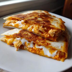 Two stacked halves of a golden-brown buffalo chicken quesadilla oozing with melted cheese and creamy sauce.