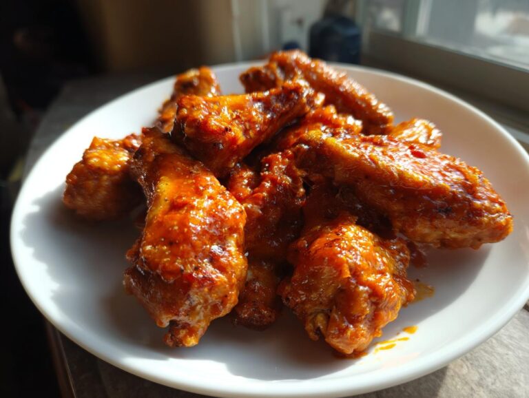 A plate piled high with glossy, saucy buffalo wings recipe pieces glistening under natural light.