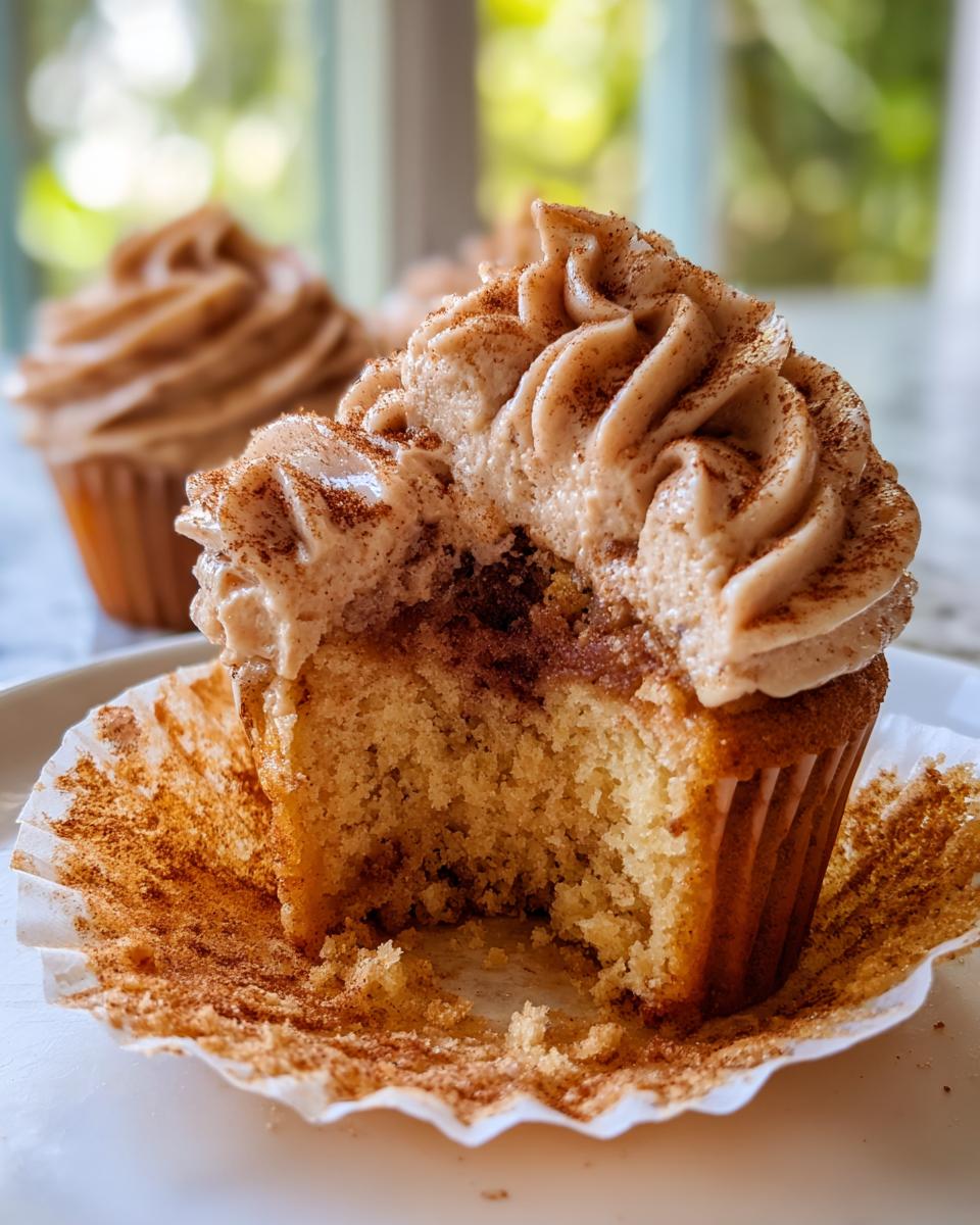 Close-up of a churro cupcake with a bite taken out, showing cinnamon filling and frosting.