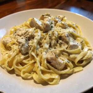 Close-up of creamy chicken fettuccine alfredo pasta topped with dried herbs on a white plate.