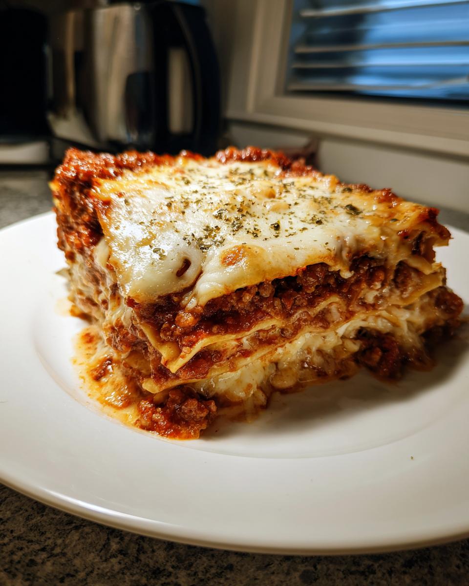 A thick, layered slice of crockpot lasagna topped with melted mozzarella and dried herbs on a white plate.