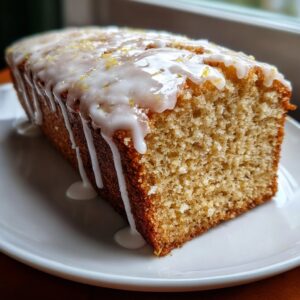 A close-up of a moist slice of eggnog bread loaf drizzled with white icing and lemon zest.